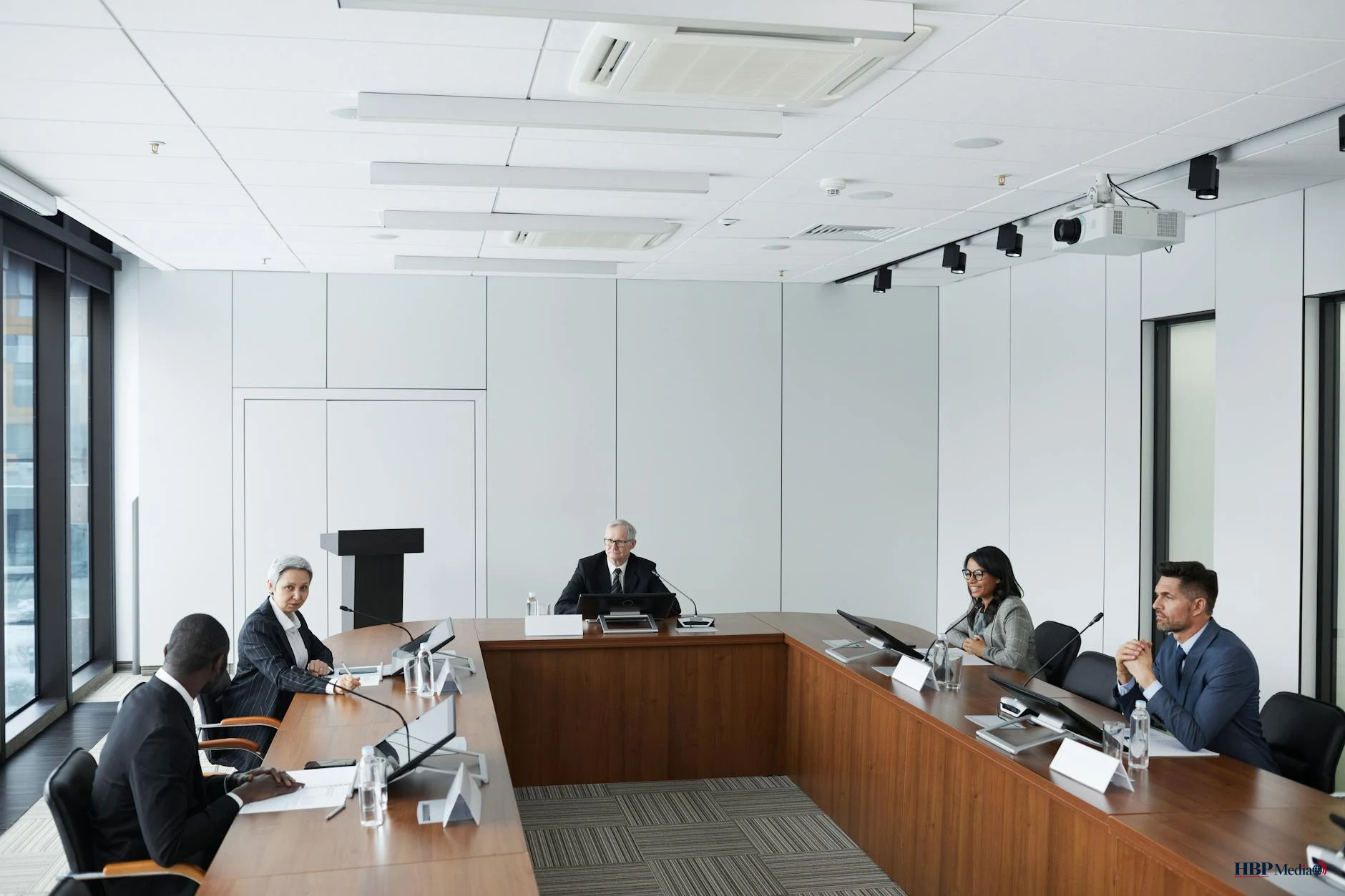 Gemeenteraadsleden tijdens een raadsvergadering in de raadzaal, onder hoge werkdruk en publieke druk