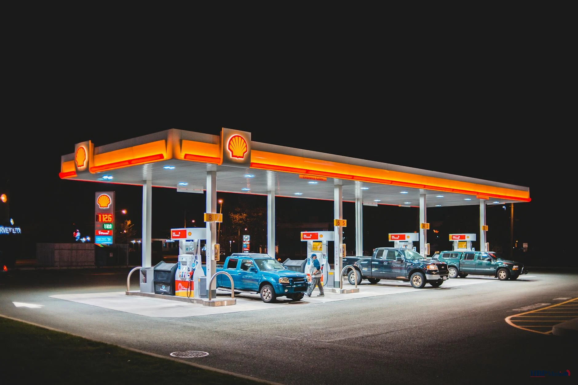 Tankstation in Nederland met automobilist die brandstof pompt — affiche toont “Prijs per liter” hoger dan verwacht bij lage olieprijs.