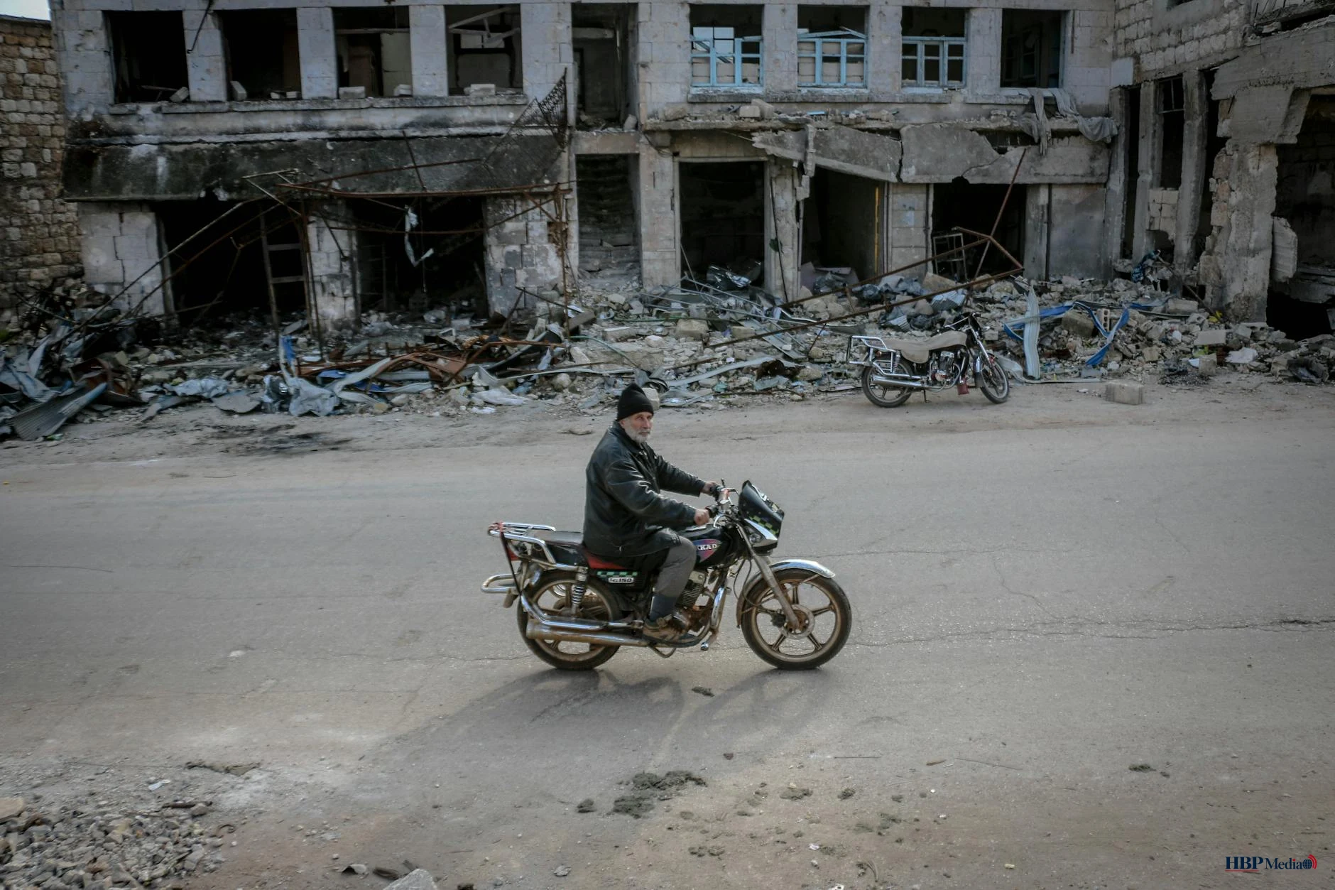 man riding motorbike along destroyed building