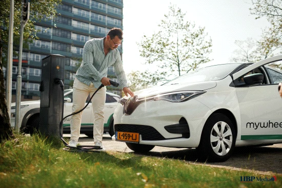 Elektrische deelauto van MyWheels geparkeerd aan een laadpaal in de stad.