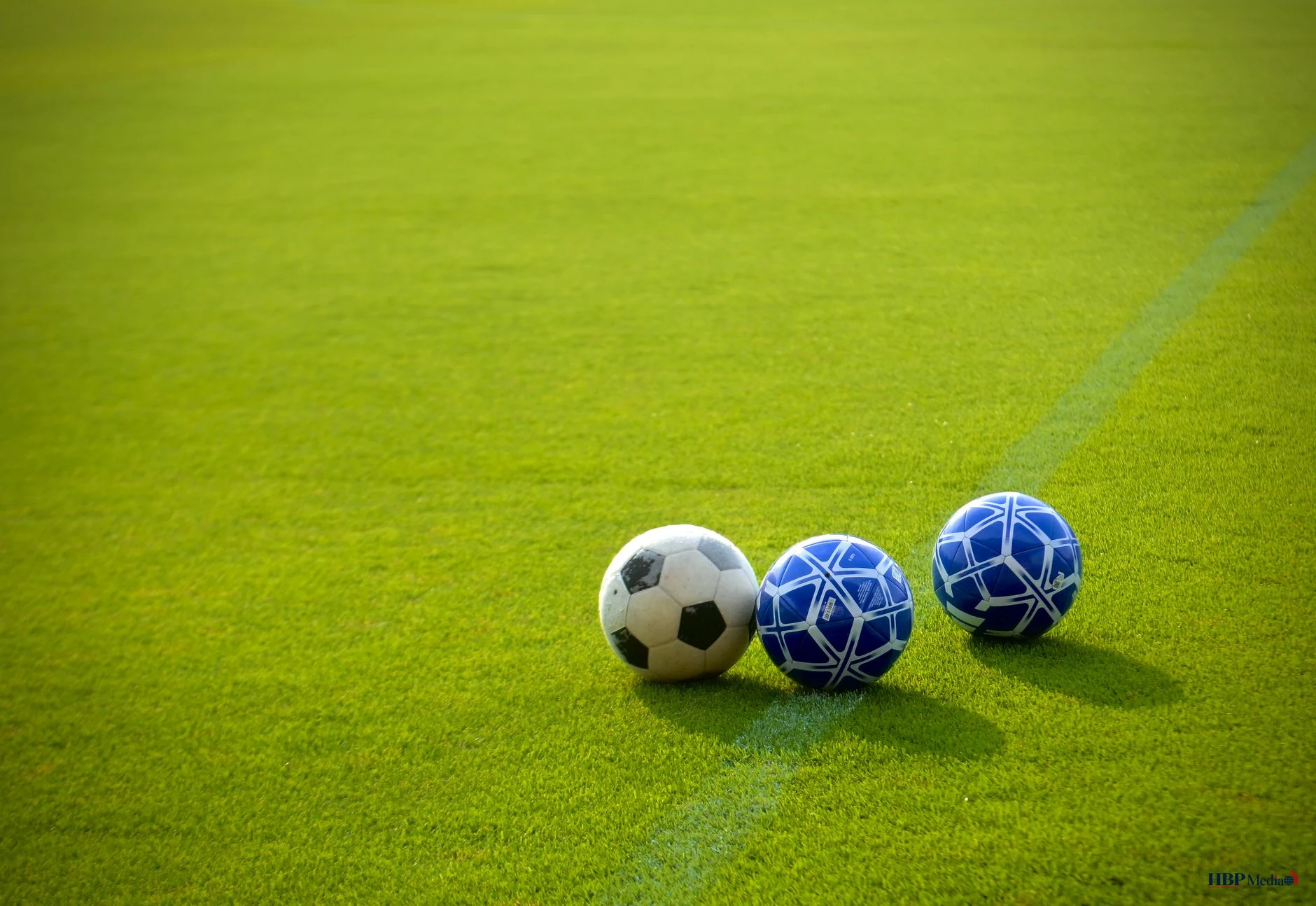 three soccer balls aligned on a lush green field