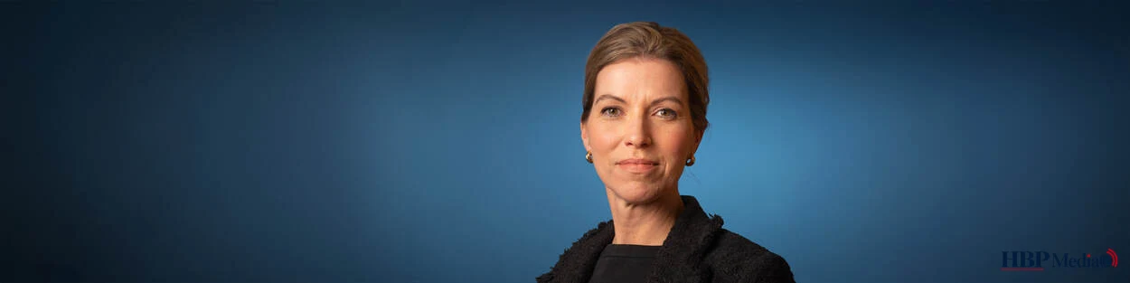Portret van staatssecretaris Claudia van Bruggen tegen een blauwe achtergrond.