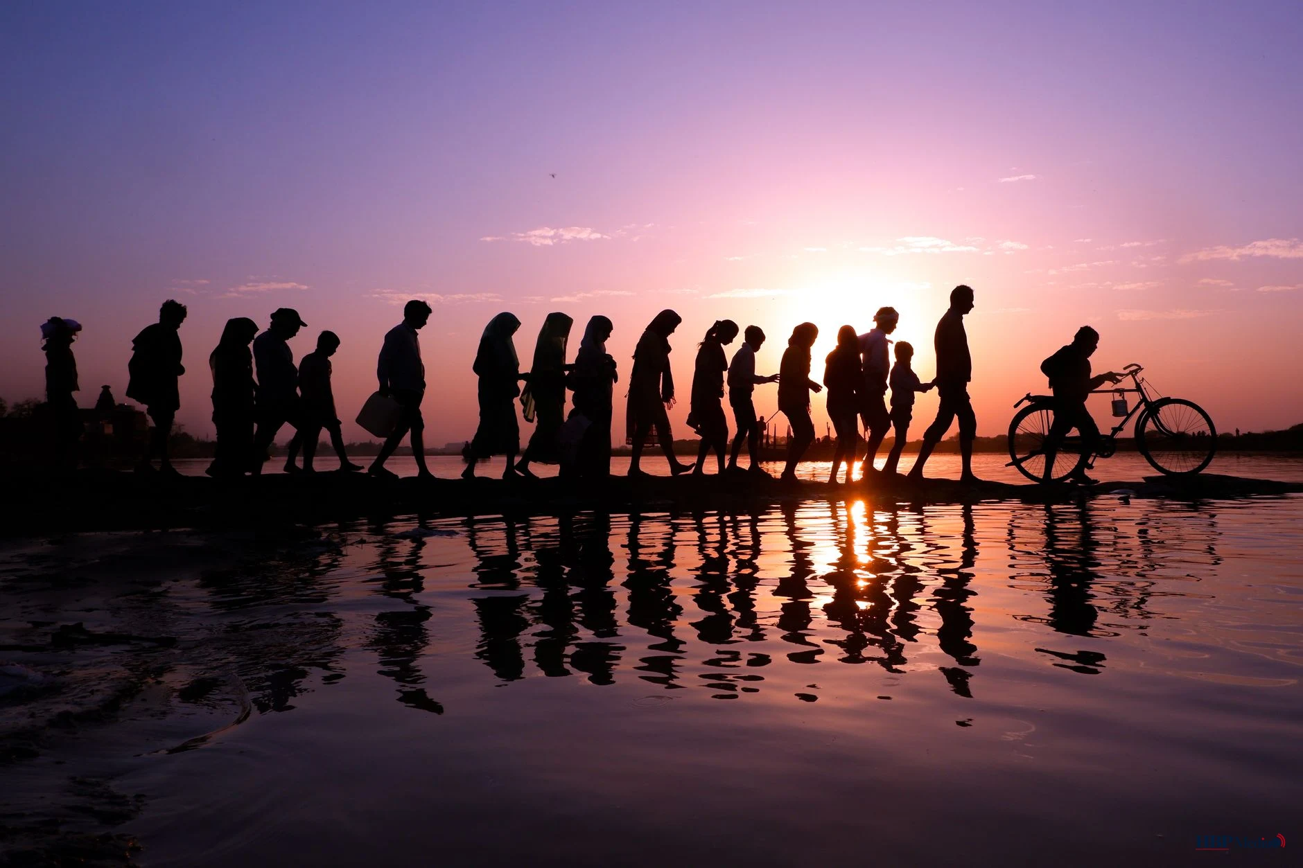 silhouetted group walking at sunset near water