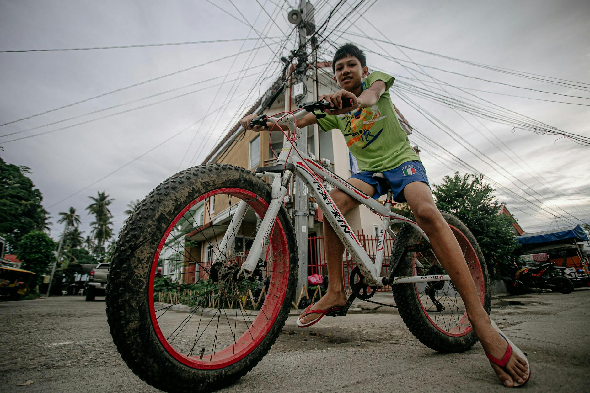 a boy in green shirt and blue shorts riding on a white bicycle